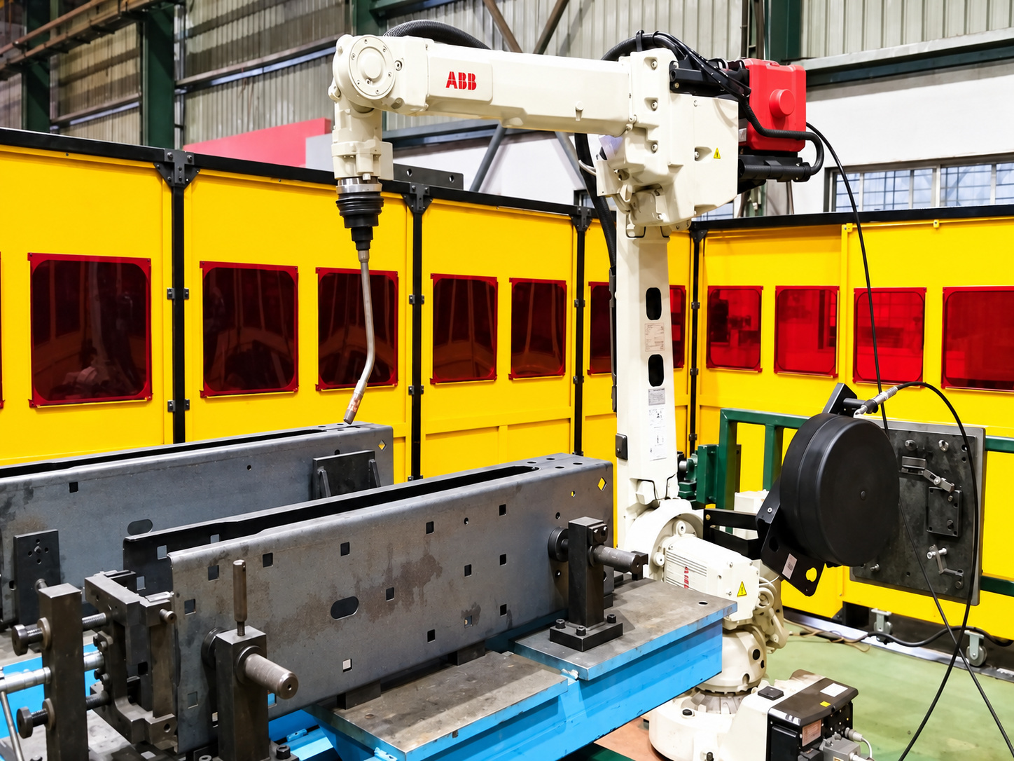 A white ABB welding robot over a steel fixture, inside a cell walled with yellow screens